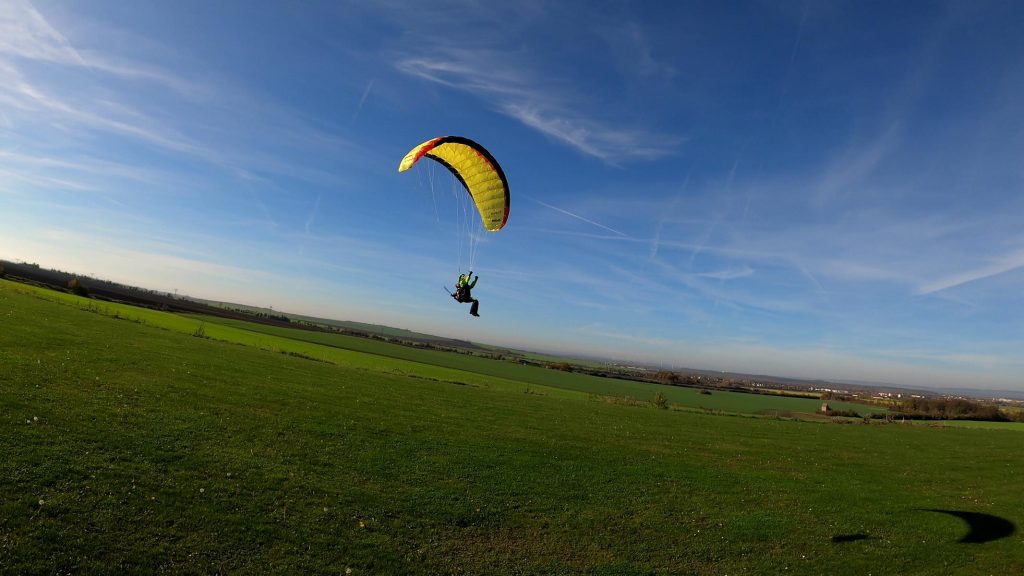 Ein gelber RC-Gleitschirm Cloud 1.0 mit einem Noah Free Set von Para Aviation RC fliegt über eine grüne Wiese, 