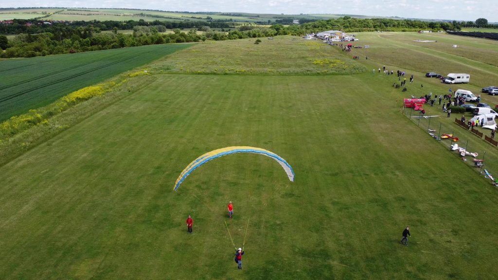 RC-Gleitschirm Phasor 2.3 RAST mit einem Piloten im Sitzgurtzeug fliegt über den Modellflugplatz des MFC Bad Langensalza. Modellpiloten stehen auf der Wiese nach dem Start