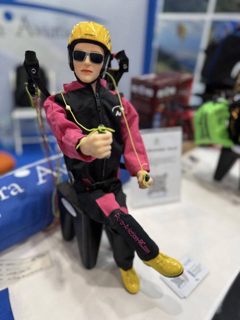 Die Para Aviation RC-Pilotenfigur „ANNA“ sitzt zusammen mit dem „Anna Free Set“ auf einem Tisch an einem Messestand.