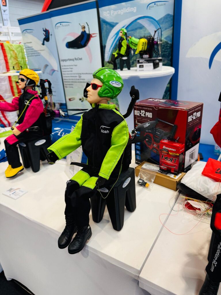 Die Para Aviation RC-Pilotenfigur „NOAH“ sitzt zusammen mit dem „Noah Free Set“ auf einem Tisch an einem Messestand.